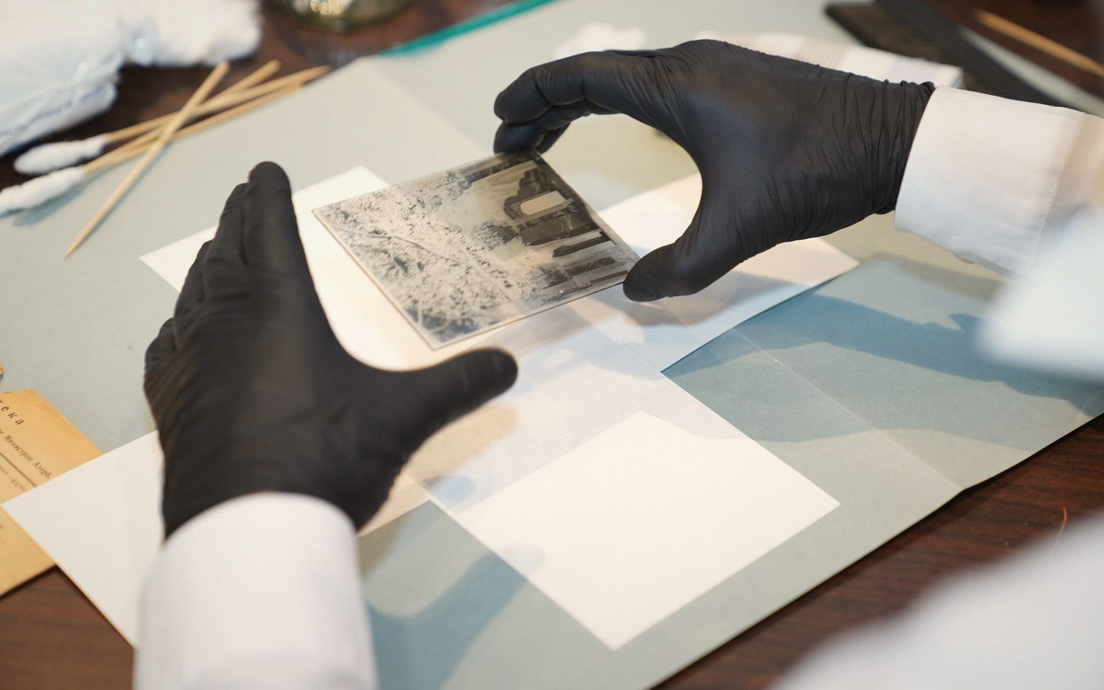 Gloved hands carefully handling an old black-and-white photograph on archival paper